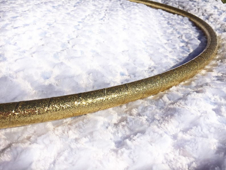 May include: A gold glitter hula hoop on a white fluffy surface.