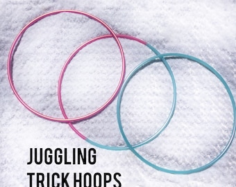May include: Three colorful juggling trick hoops. One is pink, one is teal, and the third is a lighter pink. The hoops are overlapping each other. The text "Juggling Trick Hoops" is at the bottom of the image.