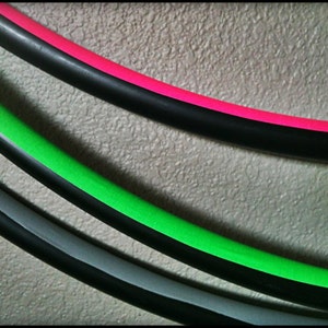 May include: Three colourful hula hoops with black, green, and pink tape. The hoops are stacked on top of each other.