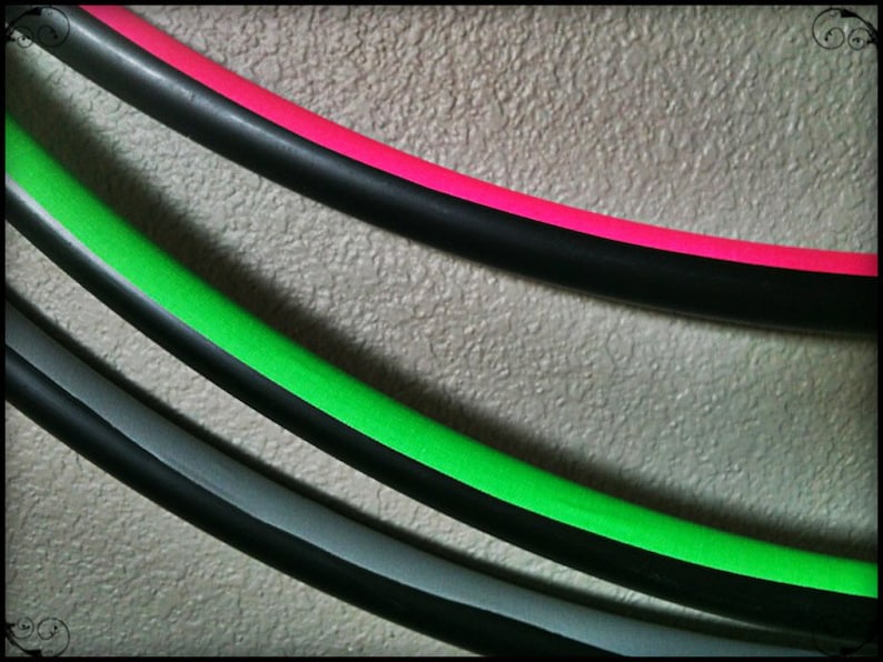 May include: Three colourful hula hoops with black, green, and pink tape. The hoops are stacked on top of each other.