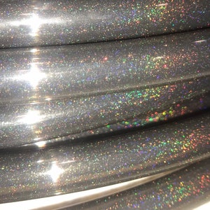 May include: Close-up of a coiled, dark grey tube with a shimmering, iridescent glitter finish. The glitter reflects a spectrum of colours, creating a sparkling effect. The tube appears smooth and flexible.