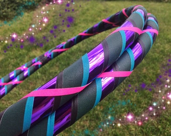 May include: A purple, teal, and black hoop with a sparkly background. The hoop is made of plastic and has a shiny finish.