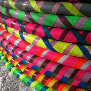 May include: A stack of colourful, striped hula hoops. The hoops are made of plastic and have a variety of colours, including pink, green, yellow, blue, and red.