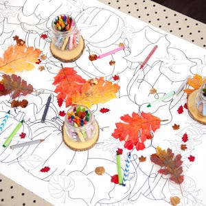 May include: A white tablecloth with a fall-themed coloring page featuring pumpkins, leaves, and vines. The tablecloth has jars of crayons and fall leaves scattered on it. The text "Happy Birthday Allie" is written on the tablecloth.