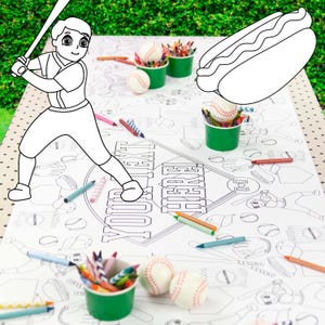 May include: A white paper coloring tablecloth featuring black line art of baseball players, hot dogs, and baseballs. The center includes a diamond-shaped graphic with the text YOUR TEXT HERE. Scattered colored pencils and baseballs are present.