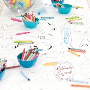 May include: A white table cloth with a shark-themed coloring page. The table is decorated with blue bowls filled with crayons and a glass bowl filled with small toys. The text "Happy 3rd Birthday Lily" is printed on the table cloth. The text "Party Melinda Bryant Boutique" is printed in a circle on the table cloth.