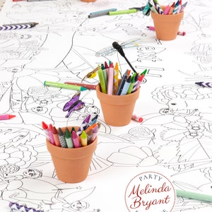 Lengthwise view of a table set with a personalized Fairy coloring banner. It is staged with crayons set in small terracotta flower pots. Craft dragonflies and butterflies on thin wires appear to hover over the pots.