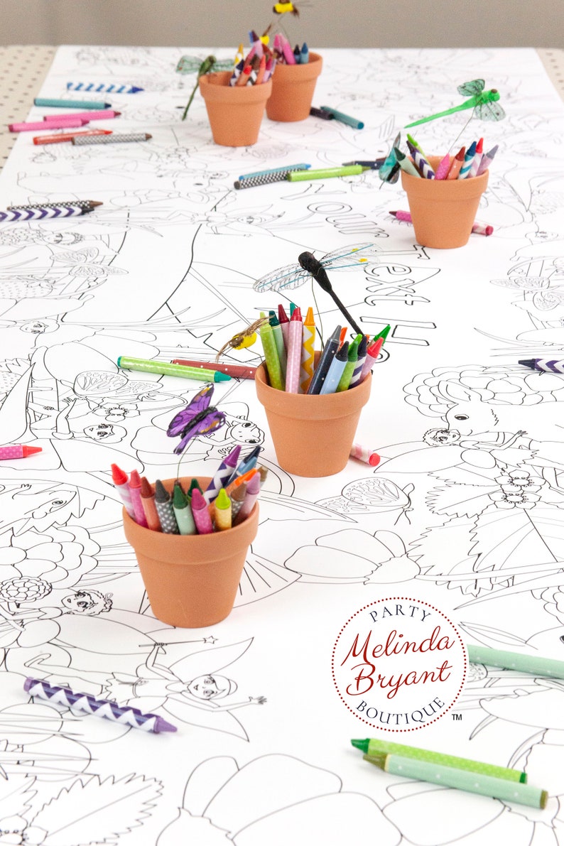 Lengthwise view of a table set with a personalized Fairy coloring banner. It is staged with crayons set in small terracotta flower pots. Craft dragonflies and butterflies on thin wires appear to hover over the pots.