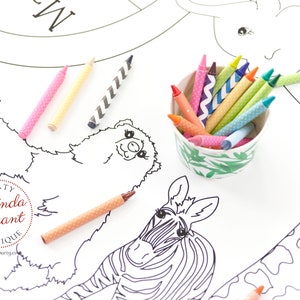 May include: A white coloring sheet featuring outlined drawings of zoo animals, including a tiger, bear, zebra, and giraffe. A small ceramic bowl filled with colorful crayons sits next to the sheet. Several crayons are scattered around the sheet.