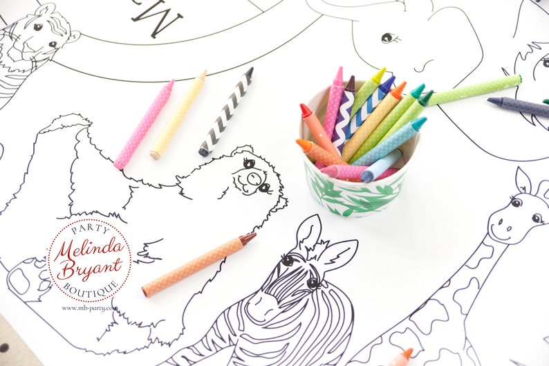 May include: A white coloring sheet featuring outlined drawings of zoo animals, including a tiger, bear, zebra, and giraffe. A small ceramic bowl filled with colorful crayons sits next to the sheet. Several crayons are scattered around the sheet.