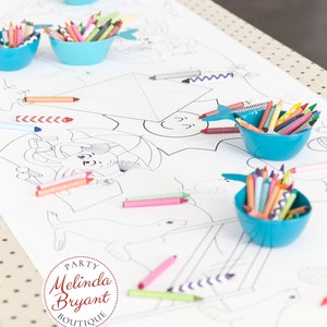 May include: A white table runner with black polka dots features a coloring page with various animal illustrations.  The table runner is decorated with blue bowls filled with colored crayons. The text "PARTY Melinda Bryant BOUTIQUE www.mb-party.com" is printed on the table runner.