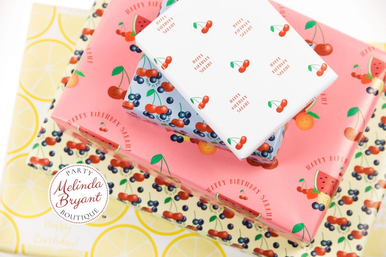 May include: Stack of three pink, white, and blue gift wrap with a lemon pattern on the bottom. The gift wrap features cherries, blueberries, watermelon, and the text "Happy Birthday Sarah".