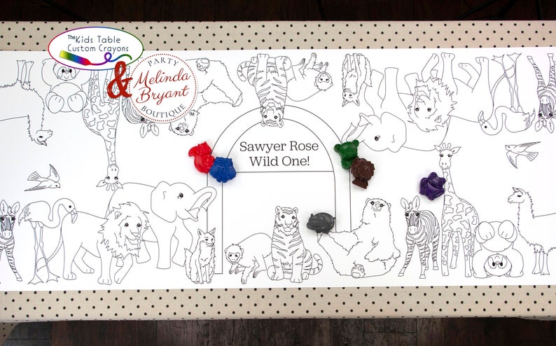 May include: White paper table runner featuring a black and white animal outline design, including a lion, giraffe, and zebra. The text "Sawyer Rose Wild One!" is in the center. Includes colorful crayons.