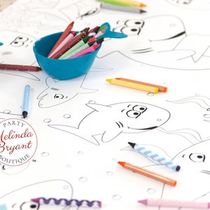 May include: A white table cloth with black outlines of sharks and other sea creatures. There are several bowls of crayons in various colors, including blue, green, red, and yellow. The table cloth has the text "PARTY Melinda Bryant BOUTIQUE TM" in a red circle.