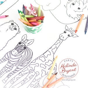 May include: A white coloring sheet featuring outlined drawings of a zebra, giraffe, and other animals. Colorful crayons in green and white patterned cups are scattered around the sheet, ready for use.