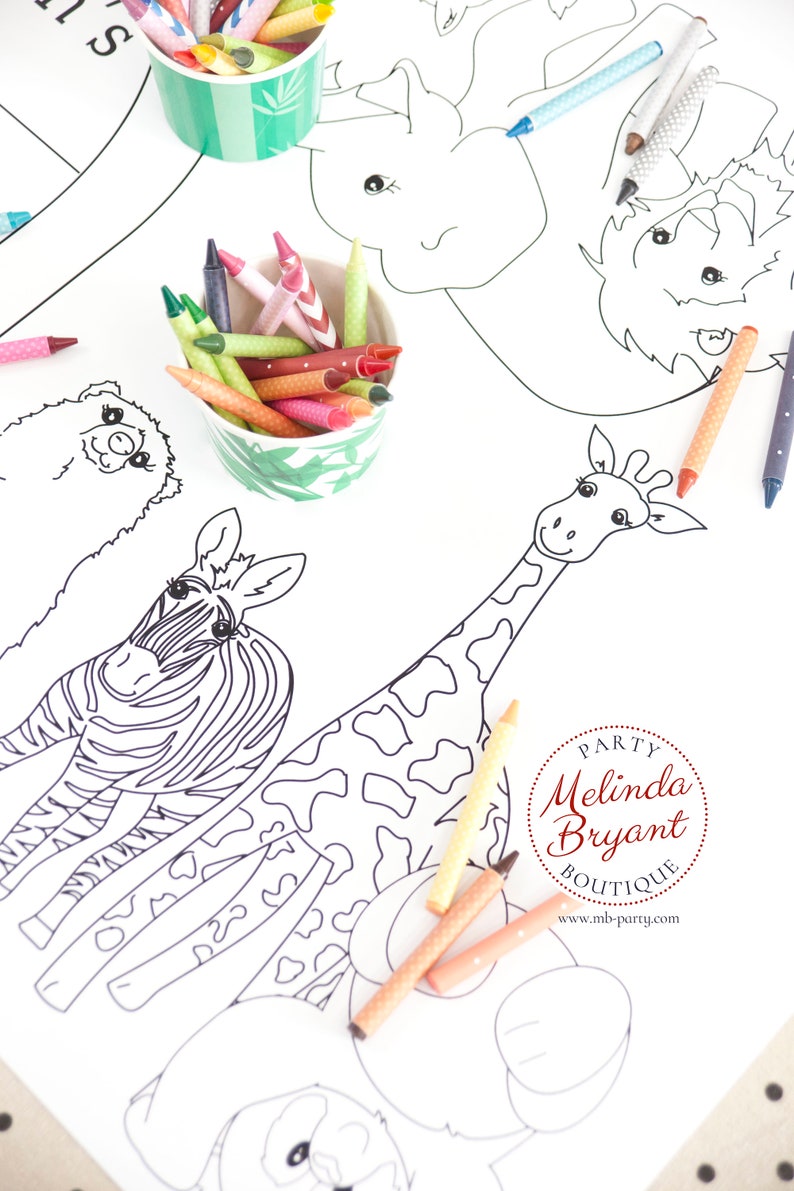 May include: A white coloring sheet featuring outlined drawings of a zebra, giraffe, and other animals. Colorful crayons in green and white patterned cups are scattered around the sheet, ready for use.