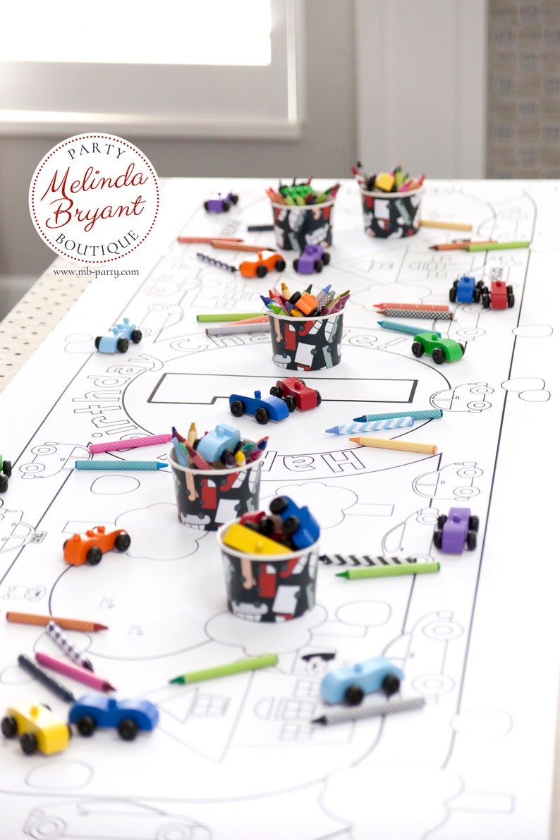 Table-length view of my personalized Cars and Trucks coloring banner. It is staged with brightly painted wooden cars and small cups filled with crayons.