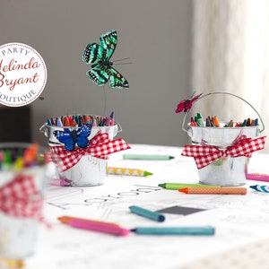Detail of suggested staging. Miniature tin milk buckets filled with crayons are tied with red and white gingham bows. Craft butterflies perch on the buckets, or fly above on thin wire.