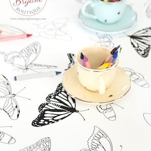 May include: A white tablecloth with black and white butterfly outlines. There are two teacups filled with crayons, one blue and one white. The text "PARTY Melinda Bryant BOUTIQUE www.mbpartyboutique.com" is printed on the tablecloth.