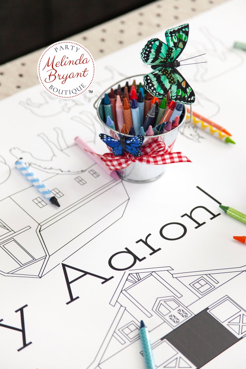 Detail showing the name Aaron, part of the custom text. Also shown: illustrations of two barns, horses, and pigs. A small milk pail filled with crayons sits on the table.