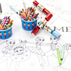May include: A white table cloth with a black and white illustration of dancers. The table cloth has the word "MERRY" printed on it. Two blue and white cups filled with crayons are on the table. Two red and silver Christmas crackers are also on the table.