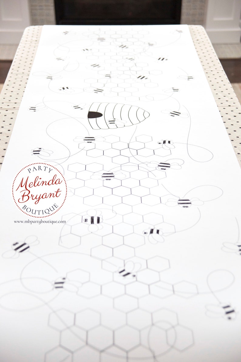 A table is set for a bee themed party or baby shower. A table length coloring page is laid over a dotted tablecloth. The design features happy bees, honeycombs, and a hive in the center. Optional text runs lengthwise along the edges. There are brightly painted honey jars filled with crayons on the table. This listing is for the coloring table runner only.