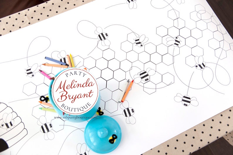 A table is set for a bee themed party or baby shower. A table length coloring page is laid over a dotted tablecloth. The design features happy bees, honeycombs, and a hive in the center. Optional text runs lengthwise along the edges. There are brightly painted honey jars filled with crayons on the table. This listing is for the coloring table runner only.