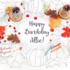Op de afbeelding: Een wit kleurtafelkleed met een herfstthema. Het tafelkleed heeft pompoenen, bladeren en de woorden "Happy Birthday Allie!" Het tafelkleed is omringd door herfstdecoraties, waaronder kleurpotloden, bladeren en potten met kleurpotloden. Het tafelkleed is van Melinda Bryant Boutique.