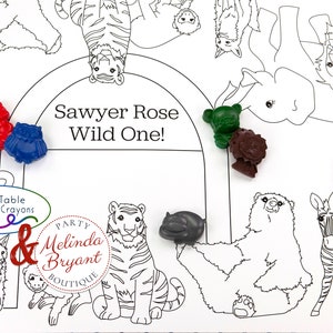 May include: A white coloring placemat with a black outline of various zoo animals, including a tiger, zebra, and giraffe. Colorful animal-shaped crayons in red, blue, green, brown, gray, and purple are scattered across the placemat. Text reads "Sawyer Rose Wild One!"