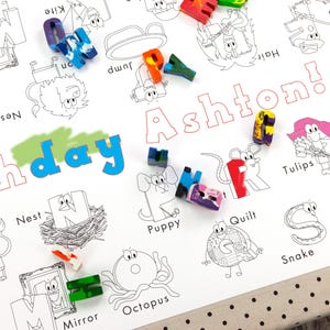 May include: A white printable birthday party activity sheet with a colorful alphabet and the words "birthday Ashton!"  The sheet features a variety of illustrations of animals, objects, and activities, such as a lion, a kite, a nest, a puppy, and a snake.