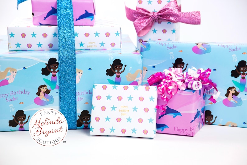 May include: A collection of gift boxes wrapped in mermaid-themed wrapping paper. The boxes are decorated with pink and blue ribbons, and the paper features images of mermaids, seashells, and stars. The text "Happy Birthday Sadie" is printed on the boxes.