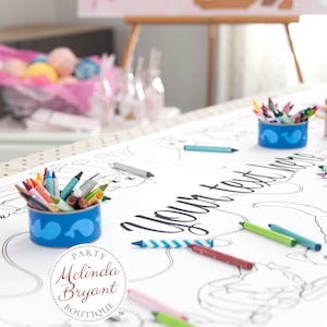 A white paper coloring table cloth with the words "Your text here" printed in black. There are crayons scattered around the table runner. There are two blue containers filled with crayons.