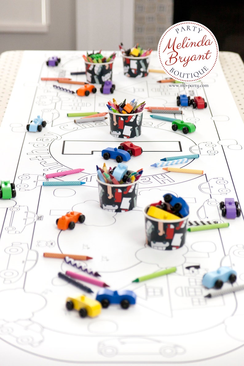 Table-length view of my personalized Cars and Trucks coloring banner. It is staged with brightly painted wooden cars and small cups filled with crayons.