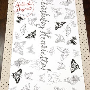 Table-length view of butterfly coloring table runner. This design is filled with line drawings of real butterflies, including Monarch and Tiger Swallowtail. Custom text in a script style font runs lengthwise down the center.