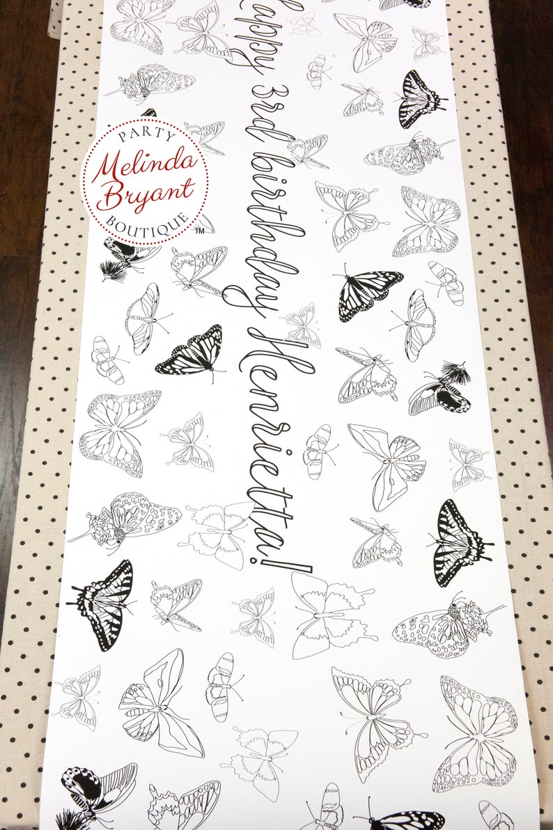 Table-length view of butterfly coloring table runner. This design is filled with line drawings of real butterflies, including Monarch and Tiger Swallowtail. Custom text in a script style font runs lengthwise down the center.