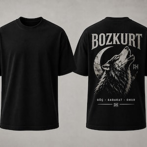 Pode incluir: Uma t-shirt preta de manga curta mostrada de frente e de costas. As costas apresentam um gráfico de um lobo a uivar perante uma lua crescente, o texto BOZKURT e as palavras GÜÇ · SADAKAT · ONUR com um símbolo rúnico abaixo do texto.