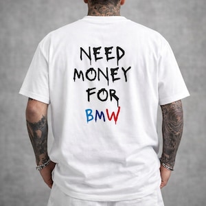 Könnte beinhalten: Weißes T-Shirt mit dem Text "NEED MONEY FOR BMW" in Schwarz, Blau und Rot. Das Shirt hat kurze Ärmel und einen Rundhalsausschnitt. Der Text ist auf der Rückseite des Shirts zentriert.