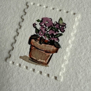 May include: A small, rectangular postage stamp featuring a watercolor illustration of a brown terracotta pot filled with purple flowers and green leaves. The stamp has a white, perforated border and is set against a textured white paper background.