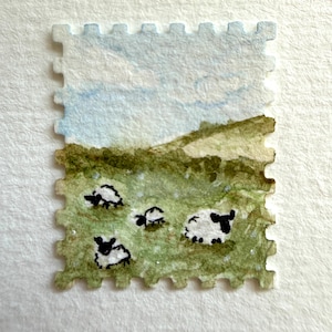 Pode incluir: Uma pintura em aquarela em formato de selo postal retangular apresentando uma paisagem pastoral com quatro pequenas ovelhas pretas e brancas pastando em um campo verde sob um céu azul claro com nuvens suaves, com borda perfurada decorativa.