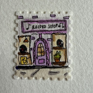 Può includere: Un francobollo con un'illustrazione disegnata a mano di un negozio di dischi con facciata viola, una porta centrale ad arco e due vetrine. L'insegna sopra la porta riporta la scritta "RECORD SHOP" con note musicali ai lati del testo.