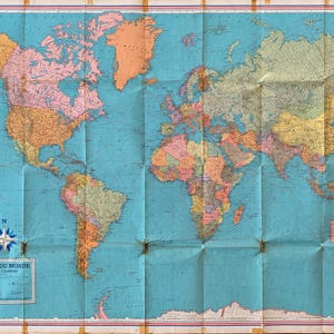 May include: A large, folded world map featuring a bright blue ocean background with continents depicted in various pastel shades of pink, orange, yellow, and green. The map includes a compass rose and a box with the text CARTE DU MONDE.