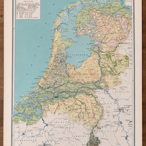 Op de afbeelding: Een vintage gedrukte kaart getiteld NEDERLAND GRONDSOORTEN met Nederland en omliggende regio's. De kaart gebruikt diverse pastelkleuren om bodemsoorten aan te duiden, met gedetailleerde zwarte tekst, grenzen en een legenda in de linkerbovenhoek.