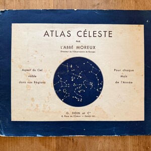 May include: A rectangular book cover titled ATLAS CÉLESTE PAR L'ABBÉ MOREUX with a dark blue border and a central circular illustration of constellations. The cream-colored background features text in French and light brown age-related spots.