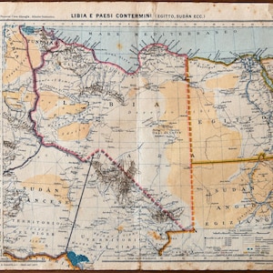 Może przedstawiać: Zabytkowa papierowa mapa zatytułowana LIBIA E PAESI CONTERMINI (EGITTO, SUDAN ECC.) przedstawiająca Afrykę Północną w wyblakłych odcieniach beżu, błękitu i bieli. Mapa ukazuje granice geograficzne, regiony pustynne i wybrzeża ze zżółkniętymi brzegami.