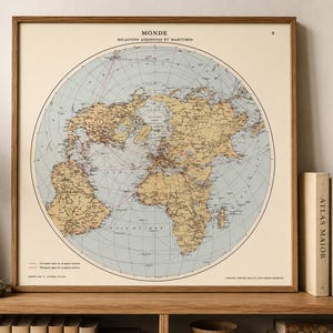 Può includere: Una stampa artistica da parete quadrata con cornice che presenta una mappa circolare del mondo in stile vintage intitolata MONDE RELATIONS AERIENNES ET MARITIMES. La mappa mostra continenti color marrone chiaro su uno sfondo blu oceano con linee rosse.