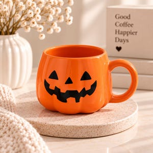 Könnte beinhalten: Ein leuchtend orangefarbener Keramikbecher in Kürbisform mit einem schwarzen Jack-o'-Lantern-Gesicht, das dreieckige Augen und einen gezackten Mund aufweist. Der Becher hat einen abgerundeten Körper und einen geschwungenen Henkel.