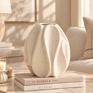Peut inclure: Un vase en céramique de couleur crème avec une finition texturée et mouchetée, présentant un design sculptural en forme de pétales avec plusieurs segments verticaux incurvés et superposés formant une silhouette organique arrondie.