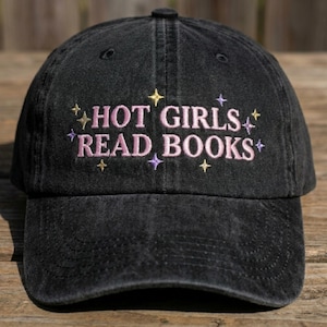 May include: Black baseball cap with the embroidered text "HOT GIRLS READ BOOKS" in pink, with gold and purple star accents. The cap is made of a worn, faded fabric.