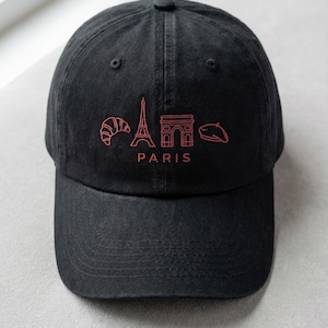Puede incluir: Gorra de béisbol negra con diseño bordado en rojo con temática parisina. Presenta un cruasán, la Torre Eiffel, el Arco del Triunfo y una boina. La palabra "PARIS" también está bordada en rojo.