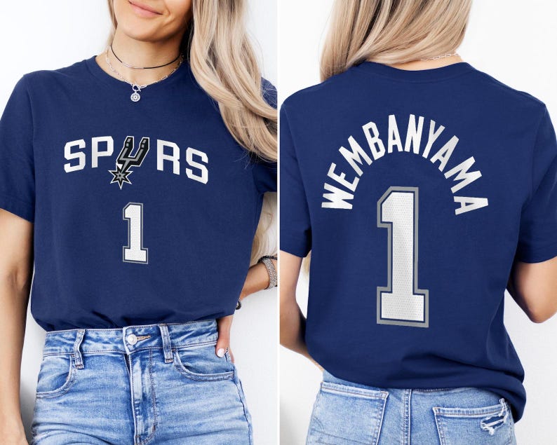 Op de afbeelding: Marineblauw T-shirt met het woord "SPURS" en het nummer "1" in het wit. Het Spurs-logo is ook afgebeeld. De achterkant van het shirt toont "WEMBANYAMA" boven het nummer "1".